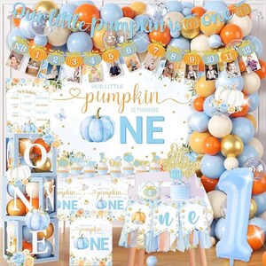 May include: A first birthday party decoration set featuring a blue and orange pumpkin theme. Includes a balloon arch, a banner with photo clips numbered 1 to 12, a table cover, a high chair banner, and a large number one balloon in light blue.