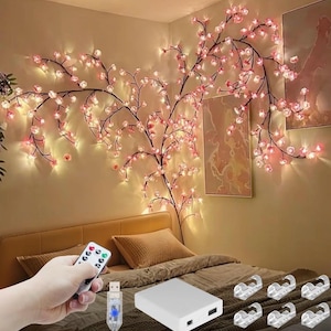 Puede incluir: Cadena de luces decorativa de flores de cerezo rosas y luces blanco cálido. Incluye un mando a distancia, un cable USB, una batería y clips de montaje. Las luces están dispuestas sobre un cable marrón oscuro.
