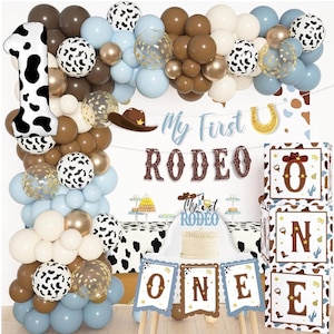 Puede incluir: Decoración de fiesta de cumpleaños con temática de rodeo con un arco de globos en marrón, blanco y azul. Incluye un globo con el número uno con estampado de vaca, una tarta y una pancarta que dice "My First Rodeo". Cajas decorativas deletrean "ONE".