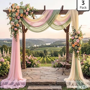 May include: A 3 Pack of sheer fabric drapes in pastel pink, sage green, and cream, hung over a wooden wedding arch. The arch is decorated with floral arrangements of peach, pink, and green roses and succulents on the left and right sides.
