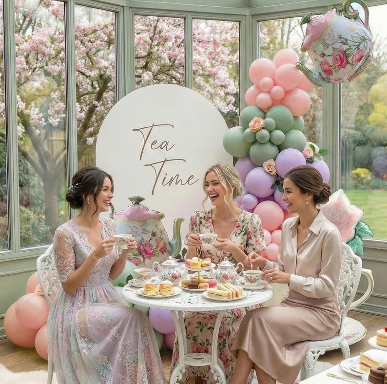 K&ouml;nnte beinhalten: Drei Frauen sitzen an einem wei&szlig;en Tisch und genie&szlig;en eine Teeparty. Auf dem Tisch befinden sich Teetassen und Geb&auml;ck. Eine Ballon-Arrangement und ein ballonf&ouml;rmiger Teekessel schm&uuml;cken die Szene. Im Hintergrund steht "Tea Time".
