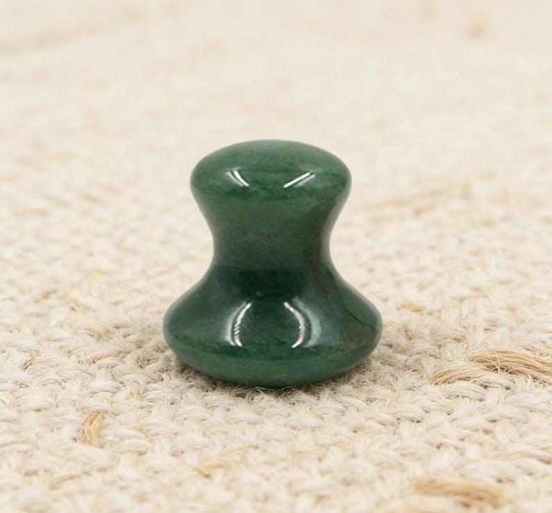 May include: A green jade gua sha tool with a smooth, rounded top and a wider base. The tool is designed for facial massage and has a polished, glossy finish. The jade is a deep, rich green color.