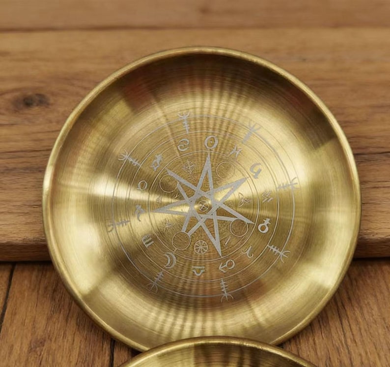 K&ouml;nnte beinhalten: Eine runde, messingfarbene Schale mit einem in der Mitte eingravierten Kompassrosen-Design. Die Schale hat eine leicht konkave Form und eine polierte Oberfl&auml;che. Die Kompassrose zeigt einen Stern und verschiedene Symbole.
