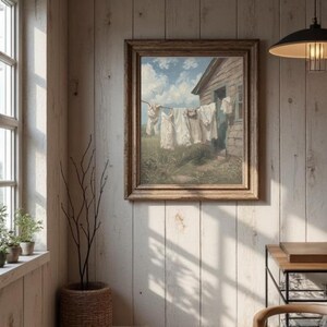 May include: A framed painting showing white laundry hanging on a washing line in front of a weathered wooden building. The scene is set in a field under a blue sky with fluffy clouds. The artwork has a vintage, rustic aesthetic.