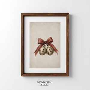 Puede incluir: Una lámina de arte enmarcada con una ilustración digital de dos cascabeles dorados metálicos atados con un lazo rojo oscuro. Los cascabeles tienen aberturas en forma de estrella y están centrados sobre un fondo beige texturizado. El texto DANYDIGITAL Art Collective aparece impreso en negro en la parte inferior.