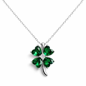 May include: A silver necklace featuring a four-leaf clover pendant. The clover is made of four heart-shaped, emerald-green gemstones, with a small diamond at the center. The chain is delicate and silver.