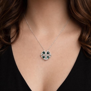 May include: Silver necklace featuring a four-leaf clover pendant. The pendant has four green gemstone leaves, each outlined with small, clear gemstones. The necklace is displayed against a dark background.
