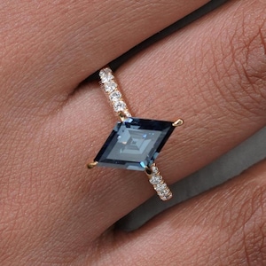 May include: A gold ring featuring a large, square-cut, dark blue gemstone. The band is adorned with small, sparkling diamonds. The ring is set on a finger, showcasing the intricate design and color contrast.