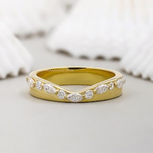 Peut inclure: Une bague en or incurvée ornée d'une rangée alternée de pierres précieuses claires de taille marquise et ronde. La bague a une finition lisse et polie et un design subtil en forme de V. Le texte "DIAMOND HUB" est visible.