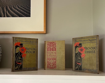 May include: Three vintage hardcover books with floral illustrations on the covers. The books are titled "New Education Readers Book Four", "Steps in English", and "New Education Readers Book Three".
