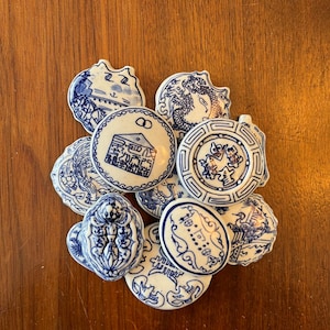 May include: A collection of ten small, round, white ceramic tiles with blue and white designs. The tiles feature various Chinese characters and symbols, including a dragon, a house, and a bird.