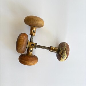 May include: Three antique wooden door knobs with brass hardware. The knobs are oval-shaped and show signs of wear, with some paint chipping. The wood has a warm, natural tone. The hardware is a mix of brass and metal.