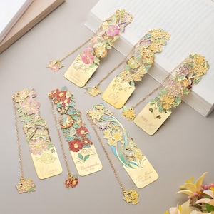 May include: Six gold-toned metal bookmarks featuring intricate cut-out floral and butterfly designs with colorful enamel accents. Each bookmark includes a matching dangling charm on a chain and engraved text, including names and dates.