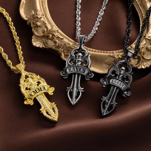 May include: Three pendant necklaces with sword-shaped designs. One is gold-toned with the name "EMMA", another is silver-toned with "RAVEN", and the third is black-toned with "CELINE". Each pendant hangs from a chain.