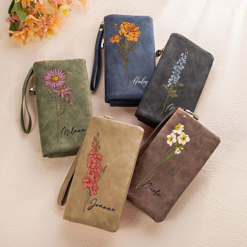 K&ouml;nnte beinhalten: Eine Sammlung von f&uuml;nf Kunstleder-Geldb&ouml;rsen in verschiedenen Farben, jede mit einem Blumendesign und einem Namen. Die Geldb&ouml;rsen sind in Gr&uuml;n-, Blau-, Beige- und Braunt&ouml;nen gehalten. Jede Geldb&ouml;rse hat eine Handschlaufe und einen Rei&szlig;verschluss.