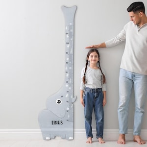 May include: A gray elephant-shaped growth chart with measurements in inches, with the name "LINUS" printed on the elephant's body. A young girl stands next to the chart as an adult measures her height.