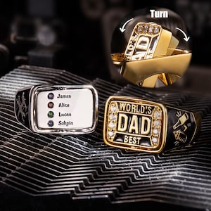 Puede incluir: Una colección de anillos personalizados. Un anillo es plateado con una cara rectangular, con nombres y piedras preciosas. Otro anillo es dorado, con "WORLD'S DAD BEST" y un gráfico de cerveza. Un tercer anillo es dorado y gira.