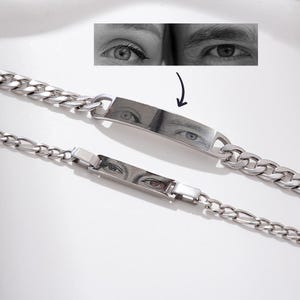 May include: Two silver bracelets with a chain link design. Each bracelet has a rectangular plate with a black and white image of eyes. The image of eyes is also shown above the bracelets.