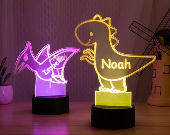 May include: Two illuminated dinosaur-shaped night lights. One is a purple Pterodactyl with the name "Isabella", and the other is a yellow Tyrannosaurus Rex with the name "Noah". Both are on black bases.