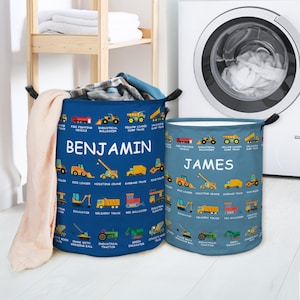 Puede incluir: Dos cestos de lavandería cilíndricos. Uno es azul marino con el nombre "BENJAMIN" en blanco, y el otro es verde azulado con "JAMES". Ambos presentan ilustraciones de vehículos y equipos de construcción, incluyendo excavadoras y volquetes.