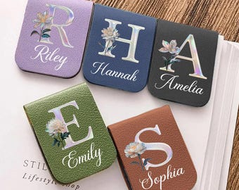 May include: A collection of personalized magnetic bookmarks in various colors: lavender, navy, black, olive green, and brown. Each bookmark features a large initial, a floral design, and a name. The names are Riley, Hannah, Amelia, Emily, and Sophia.