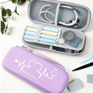 May include: A lavender medical case with a white heartbeat design and the text "Dr. K. Glover." The case is zippered and has a gray handle. Inside, a gray case holds a stethoscope, pens, and medical tools.