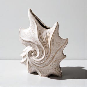 Puede incluir: Un jarr&oacute;n de cer&aacute;mica blanca con dise&ntilde;o de concha. El jarr&oacute;n tiene un patr&oacute;n en espiral y una superficie texturizada. El jarr&oacute;n mide aproximadamente 30 cm de alto.