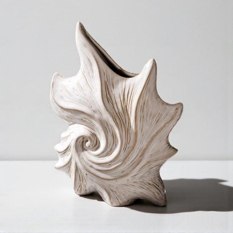 Puede incluir: Un jarr&oacute;n de cer&aacute;mica blanca con dise&ntilde;o de concha. El jarr&oacute;n tiene un patr&oacute;n en espiral y una superficie texturizada. El jarr&oacute;n mide aproximadamente 30 cm de alto.