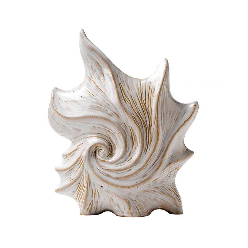 Puede incluir: Escultura de cer&aacute;mica con forma de concha. La escultura blanca presenta detalles en color beige y un dise&ntilde;o en espiral. Su superficie texturizada y forma &uacute;nica la convierten en un objeto decorativo.
