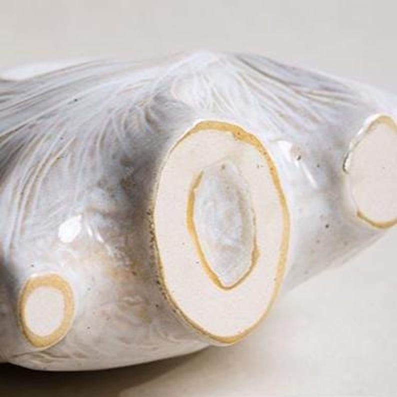 Puede incluir: Primer plano de un cuenco de cer&aacute;mica con un esmalte blanco roto texturizado. El cuenco tiene una forma org&aacute;nica &uacute;nica con un borde y una base de color marr&oacute;n claro. El dise&ntilde;o del cuenco presenta una serie de formas redondeadas y abiertas.