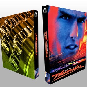 May include: Two DVD cases for the movie "Days of Thunder." One case features a close-up of Tom Cruise's face with a red and blue color scheme. The other case shows race cars and the word "Wheaties."