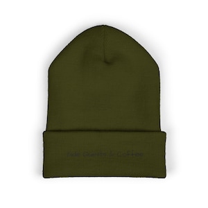 May include: An olive green cuffed beanie featuring the embroidered text Side Quests & Coffee in a dark thread color. The knit hat has a structured crown and a folded brim, showcasing a simple design with visible stitching on the front cuff.