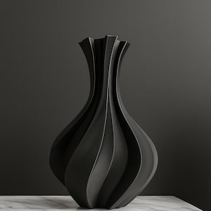 May include: A black, decorative vase with a unique, fluted design. The vase has a bulbous body and a flared, ruffled top. It sits on a white marble surface, with a dark wood cabinet below.