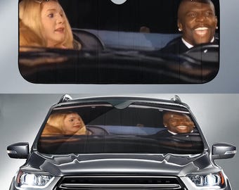 May include: Black car sunshade featuring a scene from a movie. The image shows a blonde woman and a smiling black man in a car. The sunshade is designed to fit a car windshield and protect against sunlight.