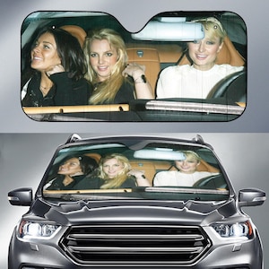 May include: Car windshield sunshade featuring a photo of three women in a car. The sunshade has a black mesh background with the image of the women smiling. The car interior is tan.