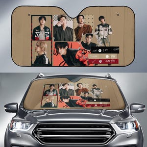 May include: Tan car sunshade featuring a collage of images of a musical group. The sunshade has a rectangular shape with a cutout for the rearview mirror. The images are arranged in a grid pattern, with the group members in various poses.