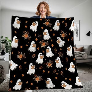 May include: A black blanket with a repeating pattern of white ghosts reading books, orange flowers, and leaves. This Halloween-themed blanket is designed to bring a spooky atmosphere to any room.