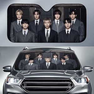 May include: Car windshield sunshade featuring a group of seven men in suits. The sunshade is black with a rectangular shape and a cutout for the rearview mirror. The men are in a formal pose, with a gray car in the foreground.