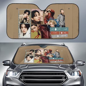 May include: A tan car sunshade featuring a collage of images of a musical group. The images are arranged in a grid pattern, with a mix of individual portraits and group shots. The sunshade is installed in a car.