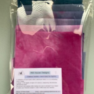 May include: A pack of fabric scraps in shades of pink, purple and blue. The pack includes a label that reads "Old House Designs" and "Fabric Variation: Colour Water Tie Dye Prints".