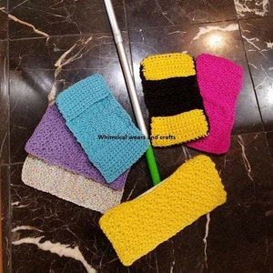 May include: A collection of colorful, crocheted cleaning pads in yellow, pink, black, blue, and purple. A silver and green mop handle is also present. The text "Whimsical wears and crafts" is visible on the blue pad.