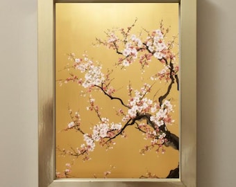 May include: A framed painting featuring a gold background and a branch of a flowering tree. The tree's dark brown branches are adorned with delicate pink and white blossoms. The frame is a light gold color.