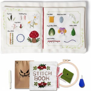 Puede incluir: Un libro de costura blanco abierto que muestra ejemplos de puntadas bordadas, incluyendo un hongo y flores. Incluye una aguja, una bolsa marr&oacute;n con una cara de monstruo, una bolsa verde y un bastidor de bordado de madera.