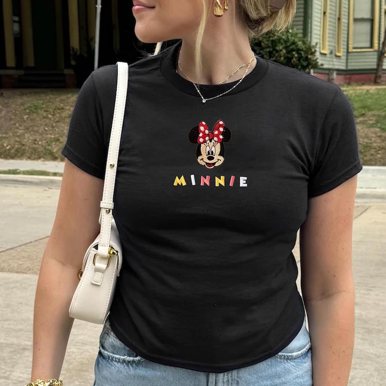 Pu&ograve; includere: T-shirt nera con un ricamo di Minnie Mouse, con un fiocco rosso a pois bianchi. La parola "MINNIE" &egrave; ricamata in lettere colorate sotto. La maglietta ha maniche corte e girocollo.