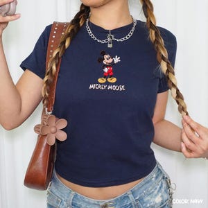 Op de afbeelding: Marineblauw T-shirt met een geborduurd Mickey Mouse-ontwerp. Het stripfiguur is afgebeeld in een rode broek, gele schoenen en witte handschoenen, met de woorden "Mickey Mouse" eronder geborduurd. Het shirt heeft een getailleerde stijl.