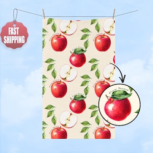 May include: A cream-colored towel with a repeating pattern of red apples, green leaves, and apple slices. The text "FUCK TRUMP" is written on the leaves. The towel is hanging on a clothesline against a blue sky.