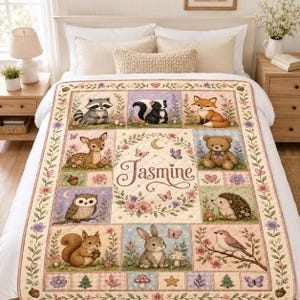 Pode incluir: Uma manta acolchoada com uma coroa de flores central com o nome Jasmine e uma lua crescente, rodeada por painéis retangulares com ilustrações de animais da floresta, incluindo guaxinim, doninha, raposa, veado, urso, coruja, ouriço, esquilo, coelho e pássaro.