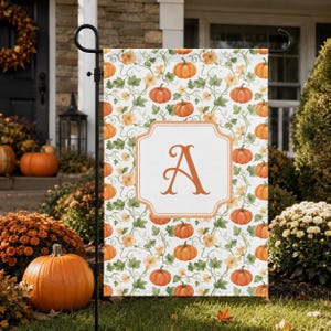May include: A rectangular garden flag featuring a repeating pattern of orange pumpkins and green vines on a white background. In the centre, a white rectangular frame with rounded corners contains a large, orange, serif-style letter A.