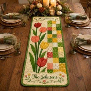 May include: A rectangular quilted table runner featuring a patchwork design of green, yellow, and red squares alongside appliqued red, orange, and yellow tulips. The runner includes the text The Johnsons at the top and bottom with floral accents.