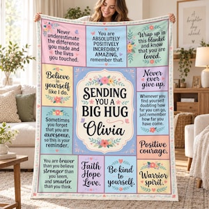 May include: A rectangular throw blanket featuring a patchwork design with pastel-colored panels. The center panel reads "SENDING YOU A BIG HUG Olivia" surrounded by floral motifs. Surrounding panels contain inspirational text and small hearts.